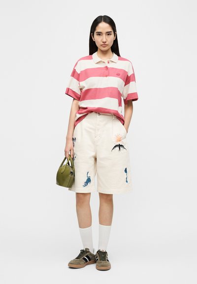 Polo rayé rose et blanc, short beige avec broderie colorée, sac à main vert, chaussettes blanches et chaussures marron avec des rayures noires.