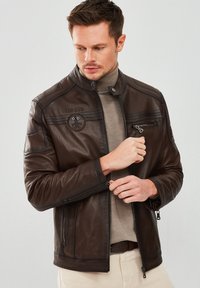 Brown leather jacket with a stand collar and zippered pockets. Features embossed "TOPGUN" logo and textured accents on the shoulders.