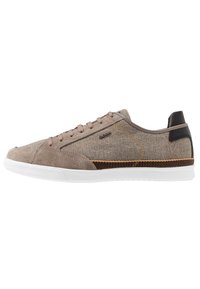 Sneaker beige con una combinazione di suede e tessuto, accenti grigi, suola bianca e tacco in texture marrone. Presenta cuciture a contrasto.