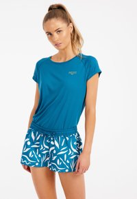 Turkossfärgad tränings t-shirt med uppvikt ärm, i kombination med mönstrade shorts med vita botaniska motiv på en matchande blå bakgrund.