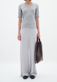 Szary T-shirt z dekoltem w serek, krótki rękaw, zestawiony z jasnoszarymi szerokimi spodniami. Czarne buty i brązowa torba dopełniają całość.