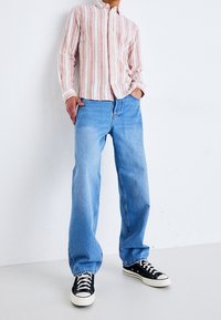 Světle růžová a bílá pruhovaná košile na knoflíky, zkombinovaná s volnými modrými džíny a černými teniskami s bílou podrážkou.