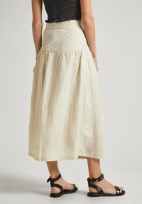 Ljusbeige midi kjol med vertikala vita ränder, utsvängd design och plisserade detaljer; matchad med svarta lädersandaler.