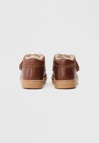 Sapatos de couro castanho com forro de pelúcia macia, apresentando uma sola de borracha bege e uma fita de ajuste em velcro para facilidade de adaptação.