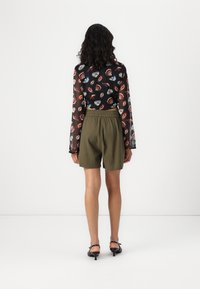 Haut noir transparent avec un motif de lèvres multicolores, associé à un short vert olive avec une taille élastique, porté avec des sandales à talons noires.