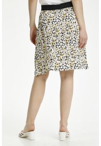 Blumenkleid mit schwarzem Grund und weißen sowie gelben Gänseblümchen, elastischem Bund und fließendem Design. Getragen mit weißen Blockabsatzsandalen.