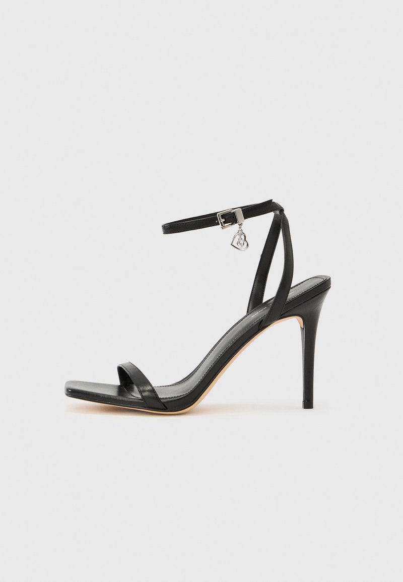 Μαύρο σανδάλι με ψηλό τακούνι, στενό λουράκι στον αστράγαλο, τετράγωνη μύτη, υλικό από λείο δέρμα και μεταλλικό διακοσμητικό πόρπη.