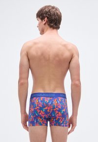 Herrenslips in Lila mit einem floralen Design in lebendigen Farben. Der Stoff ist weich und verfügt über einen breiten elastischen Bund mit Markenlogo.