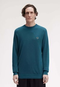 Maglione lavorato a maglia color teal con maniche lunghe, scollo a giro e polsini a coste. Presenta un piccolo logo ricamato sul petto.
