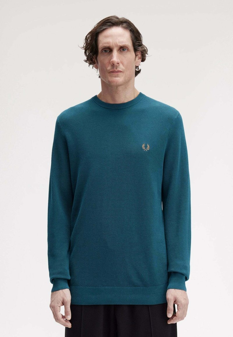Maglione lavorato a maglia color teal con maniche lunghe, scollo a giro e polsini a coste. Presenta un piccolo logo ricamato sul petto.