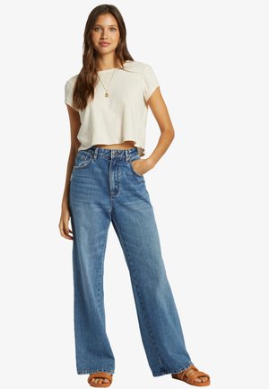 Cream cropped t-shirt, high-waisted blue wide-leg jeans, and tan sandals. Natural fabric texture; relaxed fit; visible stitching and pockets.