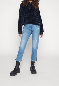 Maglietta a maniche lunghe a righe navy con collo a bottoni, abbinata a jeans in denim leggeri e strappati di colore blu chiaro e stivali alla caviglia neri con tacco.