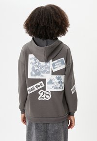 Grijze hoodie met een grote grafische print van foto's en tekst. Hoodie-ontwerp met ribgebreide manchetten en zoom. Duurzaam katoenmixmateriaal.