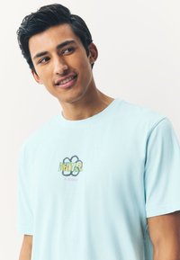 Hellblaues Baumwoll-T-Shirt mit einem bunten "Nirvana In Bloom"-Motiv auf der Brust, kurzen Ärmeln und rundem Kragen.