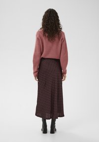 Suéter rosa con textura acanalada vestido sobre una falda midi marrón con lunares. Botas negras de tacón alto completan el conjunto.