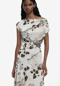 Abito senza spalle a più motivi in tessuto leggero, caratterizzato da tonalità terrose di bianco, nero e marrone, con un design drappeggiato e dettagli testurizzati.