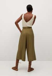 Kremowy prążkowany top na ramiączkach z głębokim dekoltem na plecach, połączony z oliwkowymi spodniami o szerokich nogawkach. Brązowe sandały na sznurowadła dopełniają stylizację.