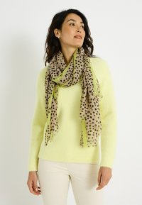 Suéter de punto amarillo claro combinado con una bufanda beige translúcida con lunares negros y bordes verdes. Textura suave con extremos con flecos.