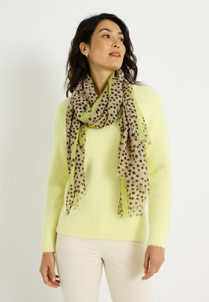 Suéter de punto amarillo claro combinado con una bufanda beige translúcida con lunares negros y bordes verdes. Textura suave con extremos con flecos.