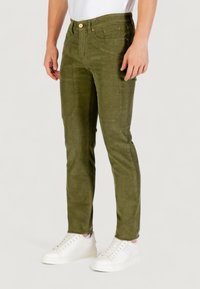 Pantaloni in velluto a coste verde oliva con una vestibilità slim, dotati di tasche frontali, bottone in vita e una texture sottile. Abbinati a sneakers bianche.