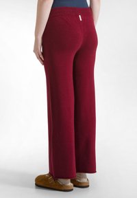 Pantalons larges bordeaux avec une texture douce et une taille élastique ; associés à des sabots marron et des chaussettes blanches, vus de derrière.