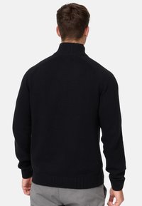 Suéter negro de punto con un cuello alto y puños acanalados. Diseño simple con un acabado texturizado, que muestra un color oscuro sólido.