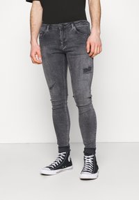 Jeans ajustados grises con desgastes en las rodillas, material de denim texturizado, combinados con zapatillas de cancha negras con suelas y cordones blancos.