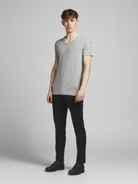 Szürke pamut V-nyakú póló fekete, slim-fit nadrággal és fekete fűzős cipőkkel párosítva. Egyszerű dizájn rövid ujjal és laza szabással.
