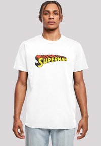 Bílý bavlněný tričko s mnohobarevným logem "Superman" v tučné retro typografii, kulatým výstřihem a krátkými rukávy.