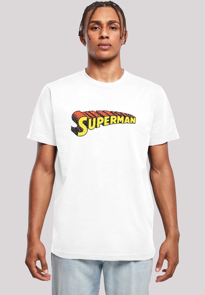 Bílý bavlněný tričko s mnohobarevným logem "Superman" v tučné retro typografii, kulatým výstřihem a krátkými rukávy.