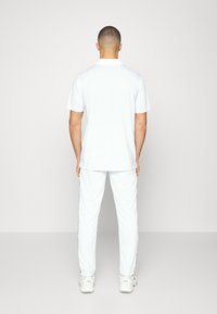 Bílá polo košile a kalhoty, s krátkým rukávem, límečkem a volným střihem. Hladká textura, jednuduchý design, doplněné o bílé tenisky.