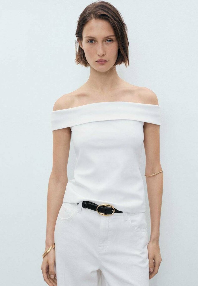 Witte off-the-shoulder top van gladde stof, gecombineerd met witte broek en een zwarte riem met een gouden accent. Eenvoudig ontwerp, geen patronen.
