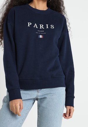 Felpa blu marina con la scritta "PARIGI" in bianco e un piccolo design della bandiera francese. Presenta un collo a giro e polsini a costine. Vestibilità casual.