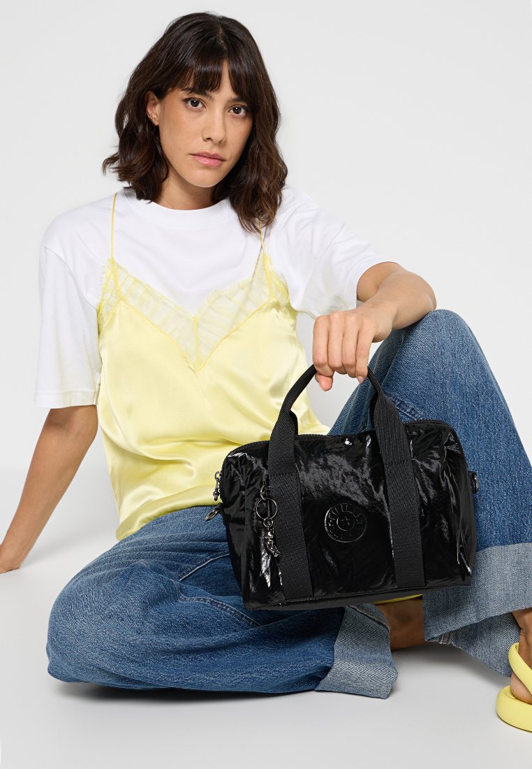 Borsa in nylon nera con texture opaca a contrasto, doppie maniglie superiori, patch circolare con logo e un accento a forma di portachiavi. Design leggero e compatto.