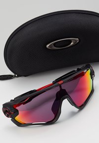 Occhiali da sole sportivi con montatura nera e rossa, lenti specchiate a sfumatura e design strutturato. Include una custodia protettiva nera.