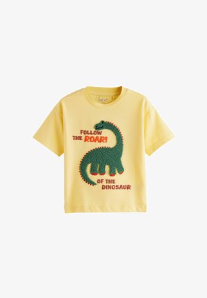Maglietta di cotone gialla con una grafica testurizzata di un dinosauro verde con accenti rossi e testo in grassetto: "SEGUITA IL RUGITO! DEL DINOSAURIO."