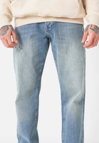 Hellblaue Jeans mit geradem Bein, die leichte Verfärbungen und absichtlich eingearbeitete Risse an den Oberschenkeln aufweisen.