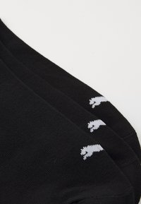 Schwarze Socken mit gerippter Textur, die oben drei kleine gestickte weiße Logos zeigen. Einfaches Design, mittellange Ausführung.