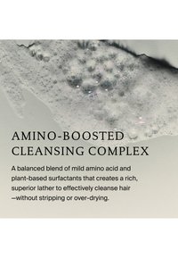 Produit nettoyant moussant sur une surface claire avec un texte décrivant un complexe enrichi en amino pour un nettoyage doux et efficace des cheveux sans dessèchement excessif.