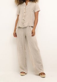 Ensemble deux pièces en lin beige clair, comprenant un haut à manches courtes avec boutons et un pantalon ample, accompagné de sandales compensées.