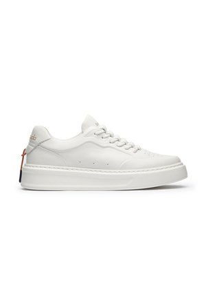 Sneaker bianca low-top con suola spessa, design con lacci, perforazioni sottili e marchio dorato vicino al tallone e alla linguetta.