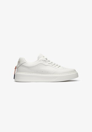 Sneaker bianca low-top con suola spessa, design con lacci, perforazioni sottili e marchio dorato vicino al tallone e alla linguetta.