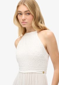 Vestito bianco senza maniche con corpino testurizzato caratterizzato da motivi geometrici e gonna svasata in tessuto trasparente. Accentatura decorativa dorata in vita.
