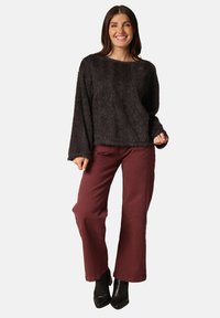 Zwarte fuzzy trui met lange mouwen, gecombineerd met bordeauxrode wijde broek en zwarte enkellaarsjes. Textuurstof, relaxte fit.