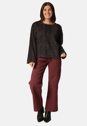 Pull noir pelucheux à manches longues, associé à un pantalon large bordeaux et des bottines noires. Tissu texturé, coupe décontractée.