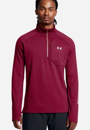 Mann in einem weinroten langärmligen Sportpullover mit Viertelreißverschluss und Brusttasche, der vor einem schlichten weißen Hintergrund steht.