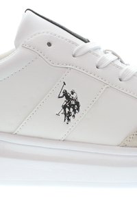 Vita sneakers med en slät läderöverdel, med en svart polo-spelare logotyp på sidan, snörning och en texturerad gummisula.