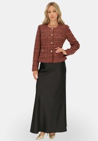 Czerwona, strukturalna kurtka z okrągłym dekoltem i złotymi guzikami, zestawiona z czarną spódnicą do ziemi i beżowymi szpilkami.