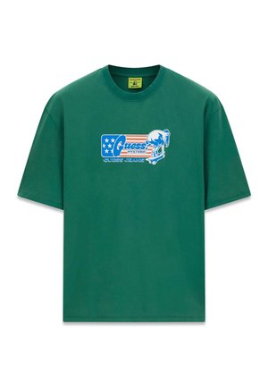 Grünes T-Shirt mit kurzen Ärmeln, blau-rotem "Guess Jeans"-Logo und einer Grafik von einer Person, die auf dem Brustbereich Skateboard fährt.
