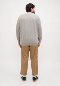 Sweat-shirt gris à manches longues et col rond, associé à un pantalon cargo beige avec poches latérales, et des baskets noires.
